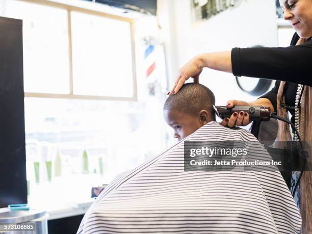 woman clipping hair of boy in retro barbershop - rasieren stock-fotos und bilder