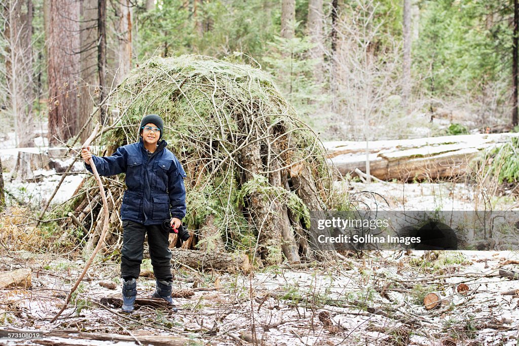 Hispanic boy building hut from branches in forest