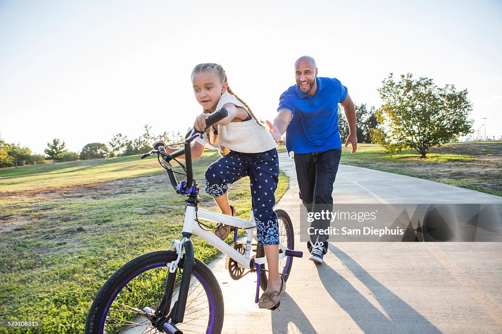 Father teaching daughter to ride bicycle in park