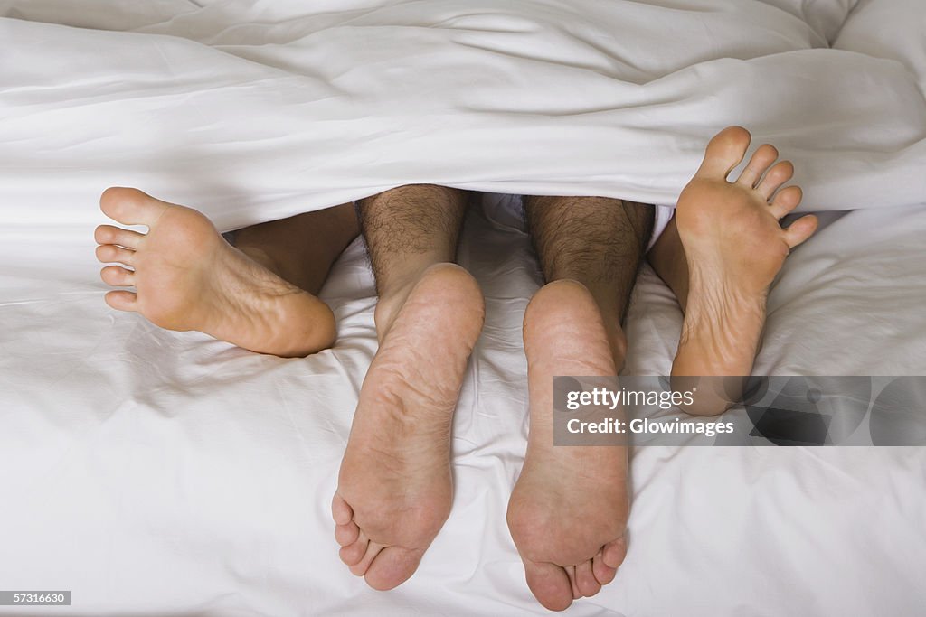 High angle view of a couple's feet under the sheets of a bed