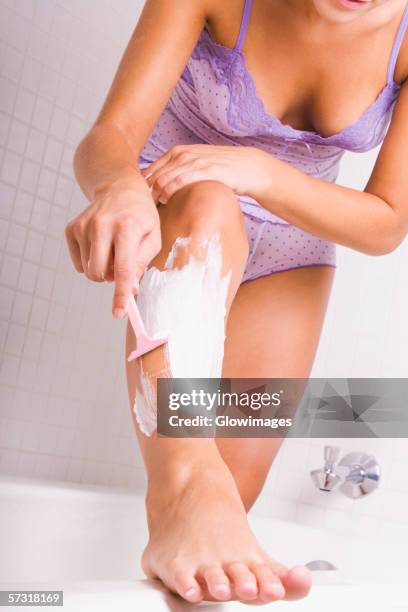 young woman shaving her legs - scheren stockfoto's en -beelden
