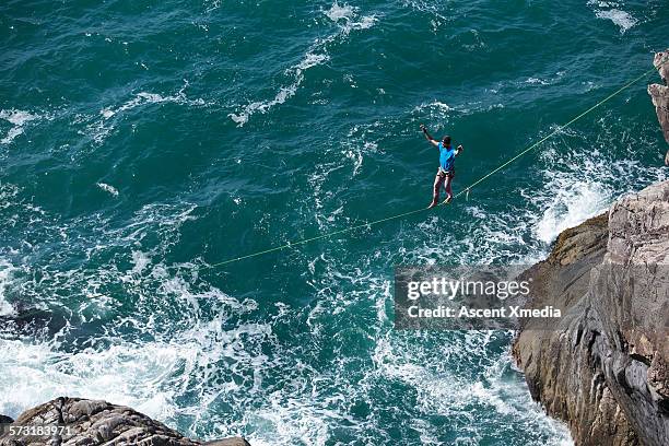 man traverses highline above ocean swell - slackline foto e immagini stock