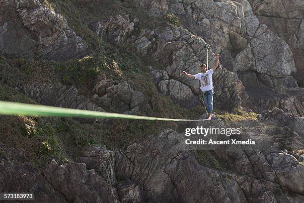 man traverses highline between rock cliffs - highline stock-fotos und bilder