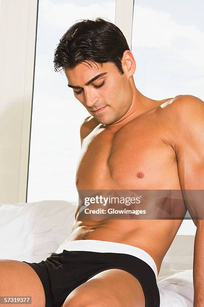 young man sitting on the bed looking down - semi dress fotografías e imágenes de stock