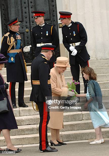 Queen Elizabeth II receives flowers as Prince Philip, Duke of Edinburgh, Prince William and Prince Harry stand together at the passing-out...