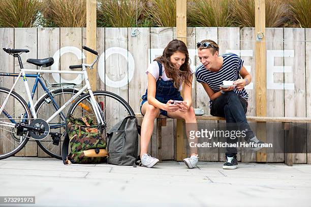 couple sitting outside cafe looking at phone - london bikes stock pictures, royalty-free photos & images