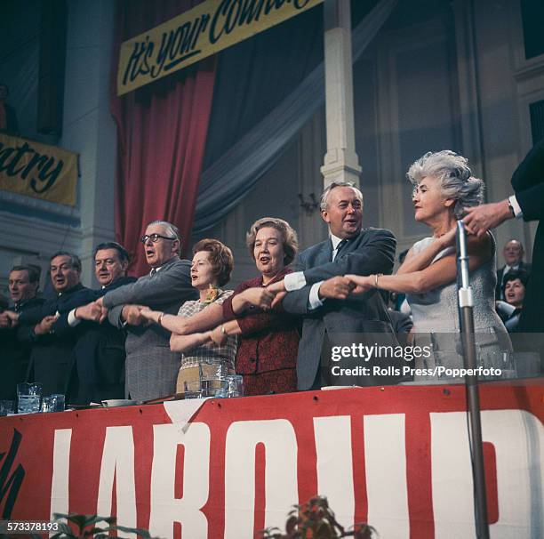 View of Labour Party politicians standing together and linking hands on the platform as they sing 'The Red Flag', the traditional song to end the...