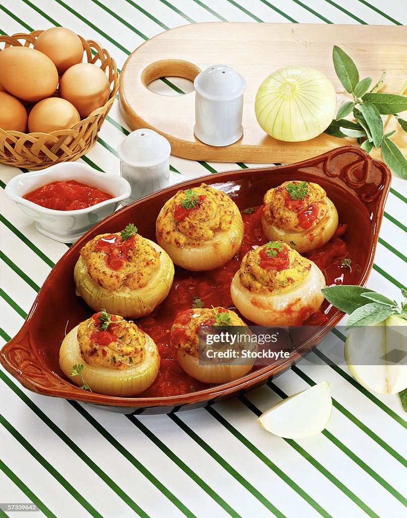 High angle view of a stuffed vegetable dish garnished with herbs kept beside a dip and white onions