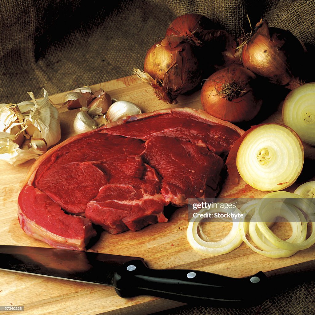 High angle view of a cut of steak on a board with onions and garlic