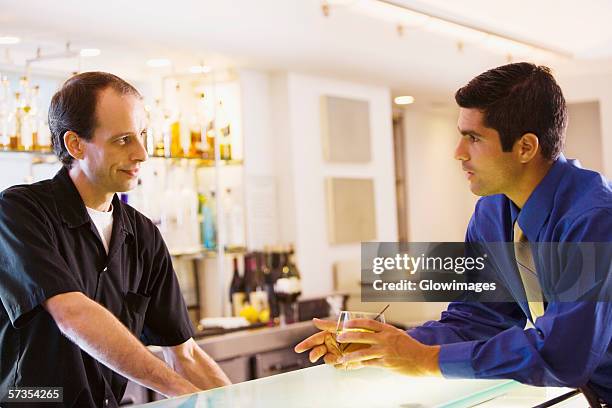 side profile of a businessman holding a glass talking to a bar tender - rietje los stockfoto's en -beelden