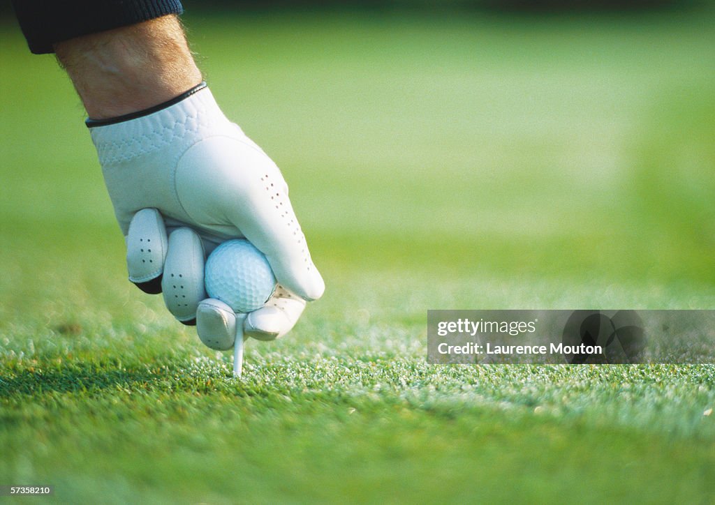 Golfer's gloved hand teeing up, close-up