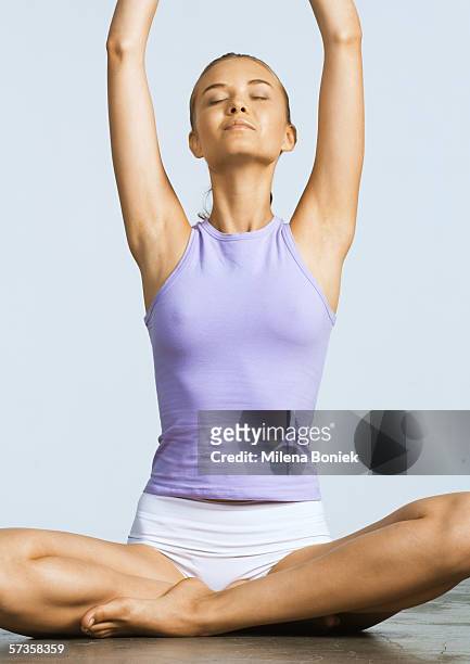 woman sitting indian style on floor with arms raised and eyes closed - leg stretch girl stock pictures, royalty-free photos & images