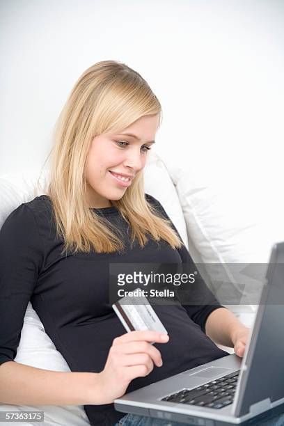young woman sitting and holding credit card in front of laptop - female 18 21 blonde blue eyes stock-fotos und bilder