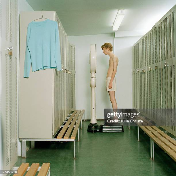 a young man standing on a scale in a locker room - delgado fotografías e imágenes de stock