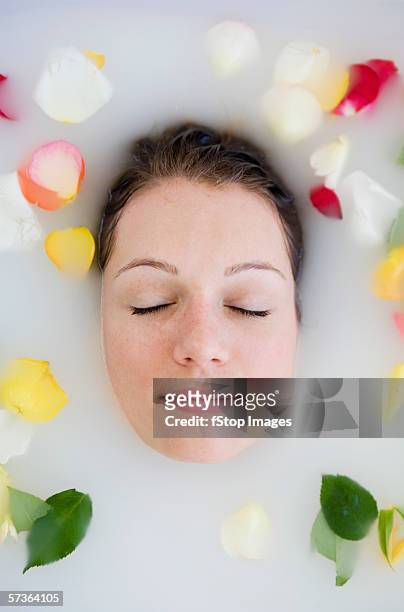 young woman with eyes closed lying in bathtub and surrounded by rose petals - white rose flower spa photos et images de collection