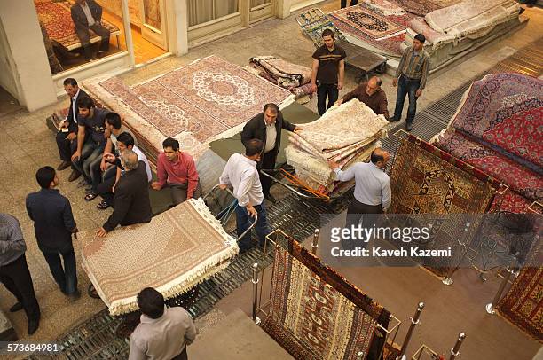 Men carry carpets on push carts in the carpet section of the grand bazaar on May 3, 2012 in Tehran, Iran. Others in the carpet business sit on stacks...