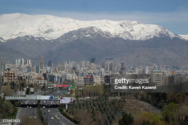 Skyline of north Tehran with hills covered in snow and the high rises scattered around and cars on Modares highway heading to the center seen on...
