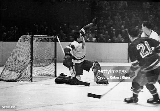 Canadian hockey player Terry Sawchuk , goalkeeper for the Detroit Red Wings, reaches high to make a save during a game against the New York Rangers,...