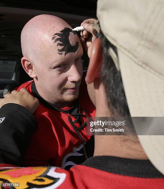 Calgary Flames fan Brad Duggan has the Flames logo painted on his forehead by friend Jason Johnson during a pre-game party in the parking lot of the...