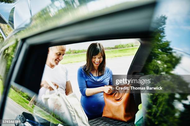 laughing pregnant couple unpacking trunk of car - chinese car home stock-fotos und bilder