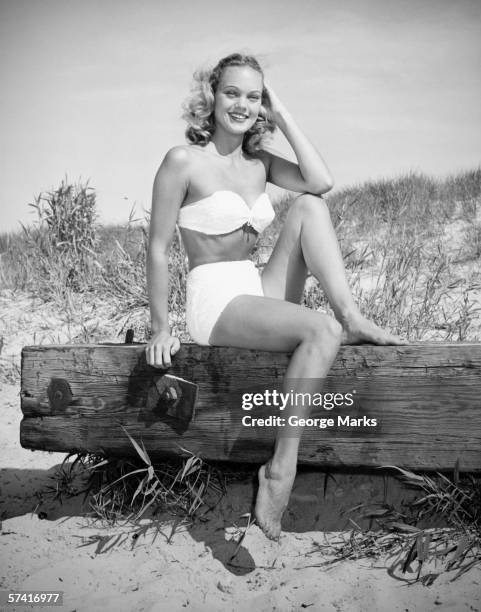 woman wearing bikini sitting on log on beach, (b&w), (portrait) - vintage glamour stock pictures, royalty-free photos & images