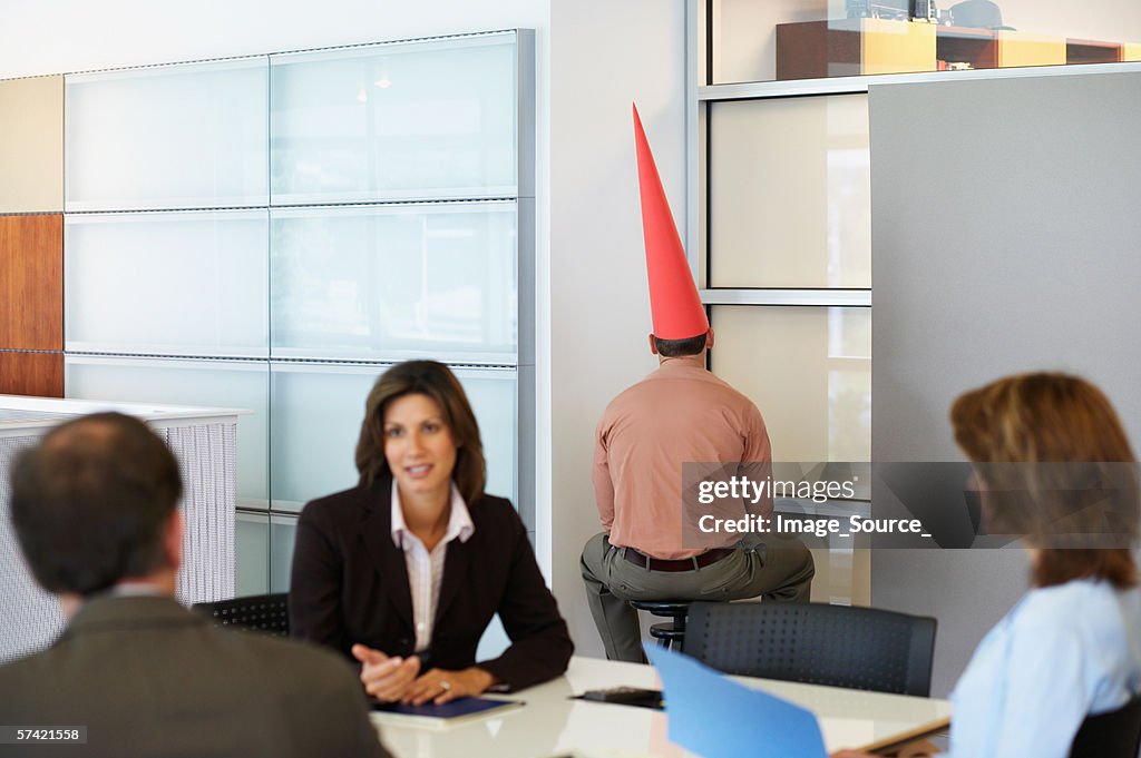 Businessman sat in corner with dunce cap