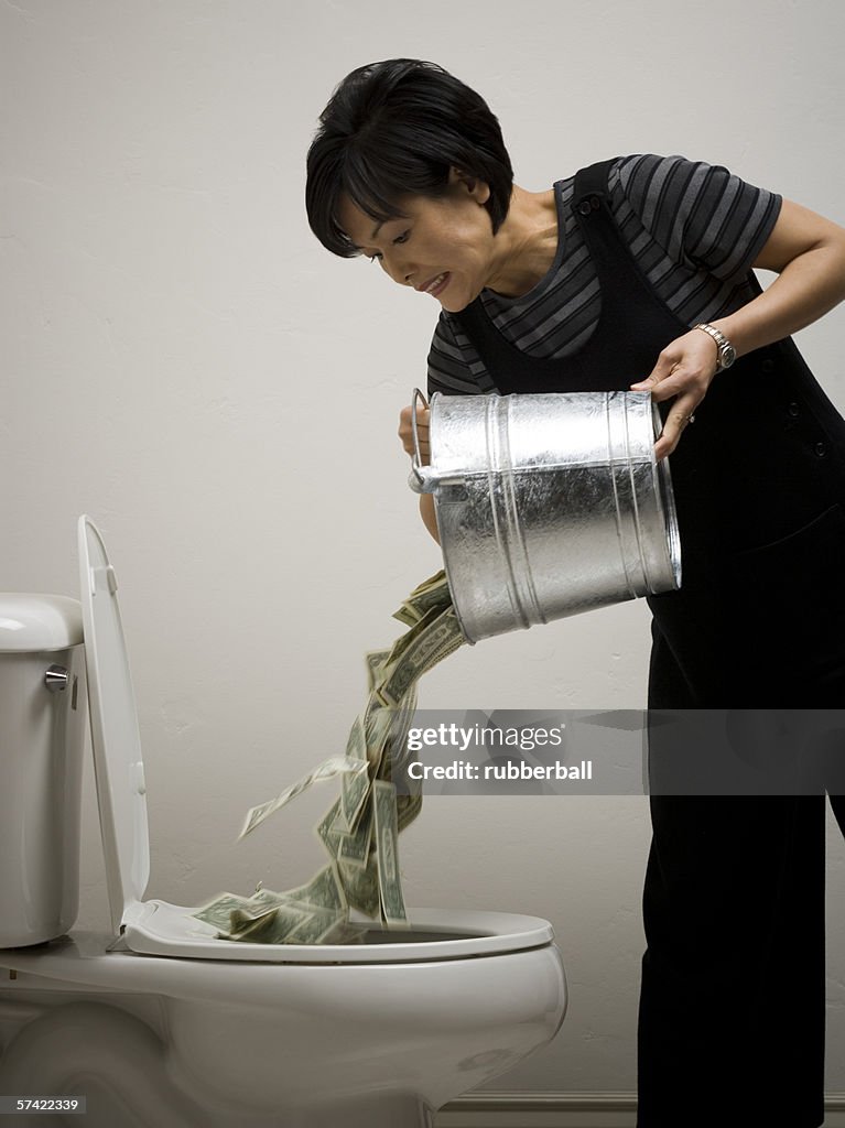 Mid adult woman emptying a bucket of money into a toilet bowl