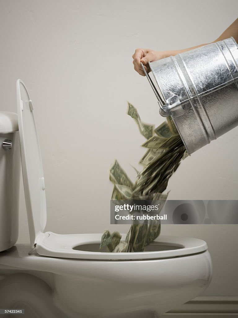 Mid adult woman emptying a bucket of money into a toilet bowl