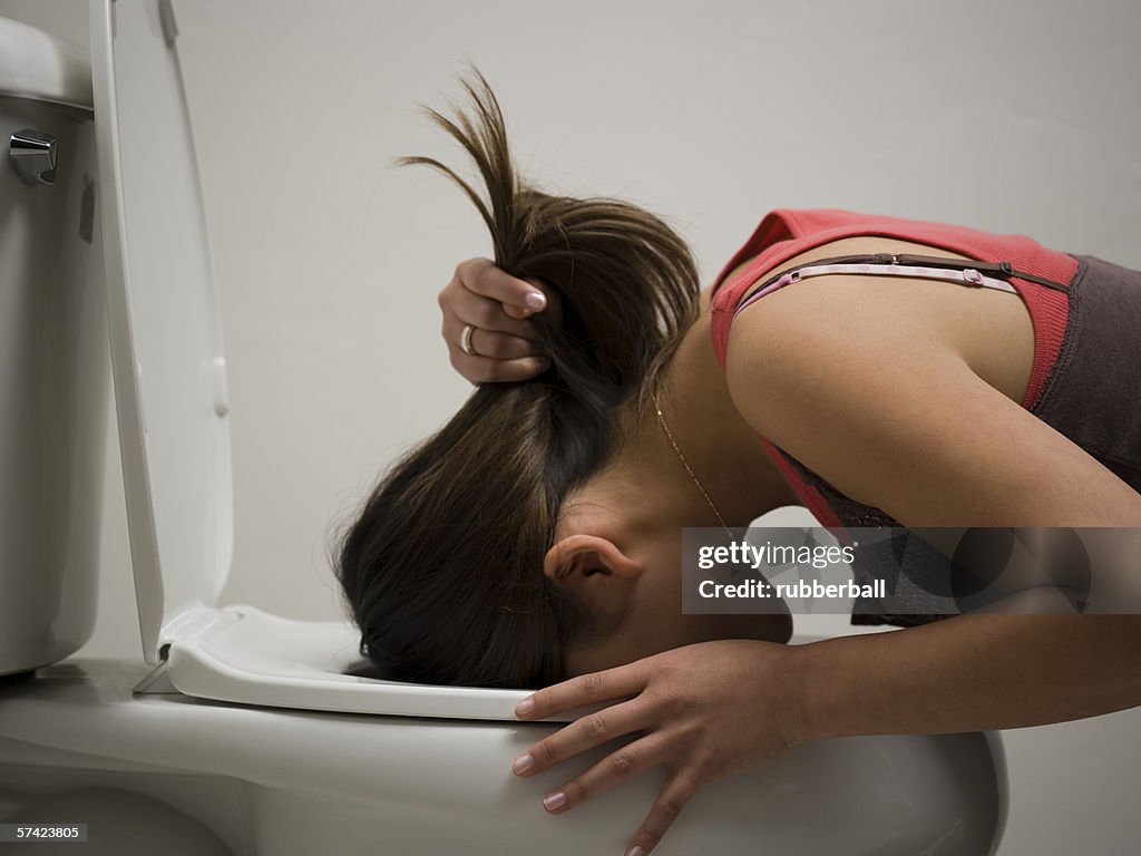 Profile of a young woman vomiting into a toilet bowl