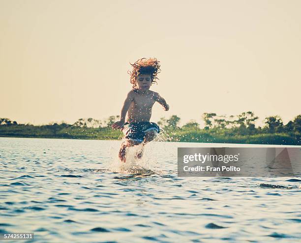 boy jumping in the water at the bay. - arschbombe stock-fotos und bilder