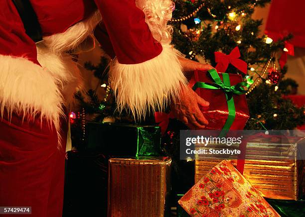 close up of santa's hands putting presents under a christmas tree - santa close up stock-fotos und bilder