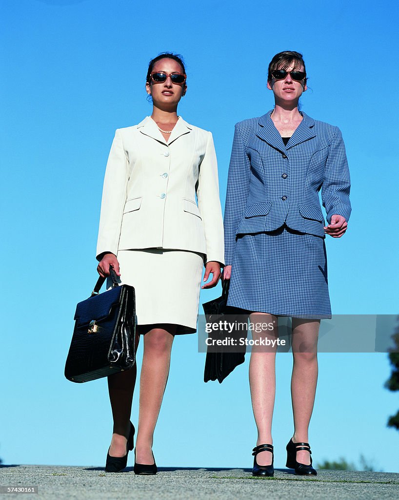 Young businesswomen walking together holding briefcases