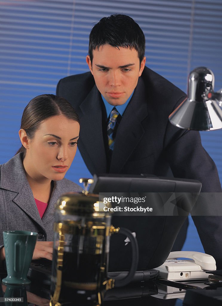 Businesswoman sitting working on laptop while businessman stands over her