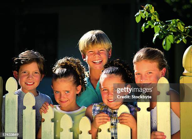 young girls and boys standing behind a picket fence - white picket gate stock pictures, royalty-free photos & images