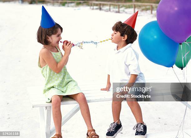 portrait of a boy and girl (6-8) at a birthday party sitting on bench and playing with streamers - birthday streamers stockfoto's en -beelden