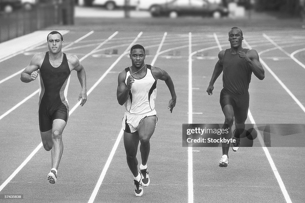 Black and white shot of three male athletes running a race on the track