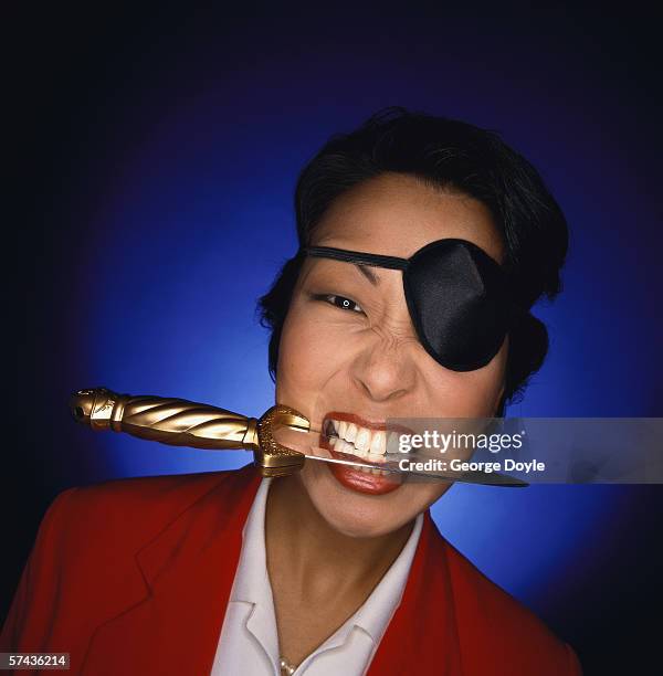 close-up of a woman wearing an eye patch and holding a knife between her teeth - business woman in red suit jacket stock pictures, royalty-free photos & images