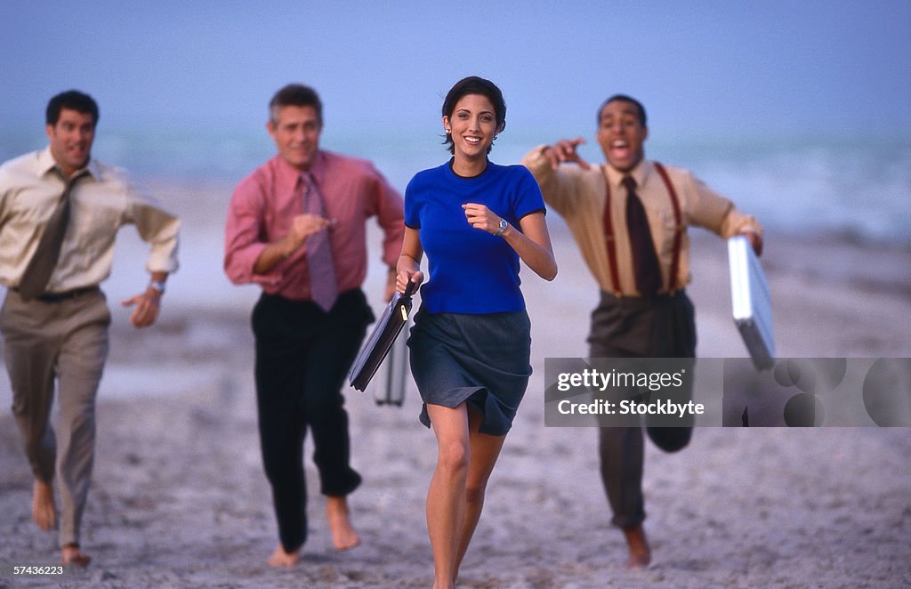 View of a group of businessmen and a woman running on the beach