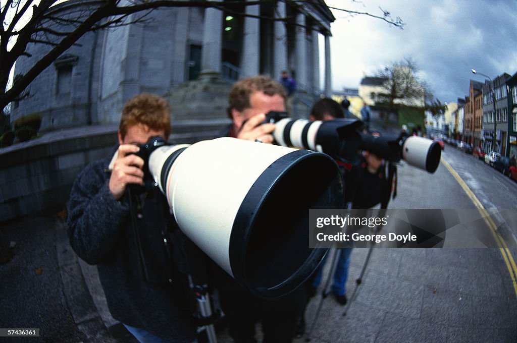 Side profile close-up of lenses on the cameras of photographers on a street