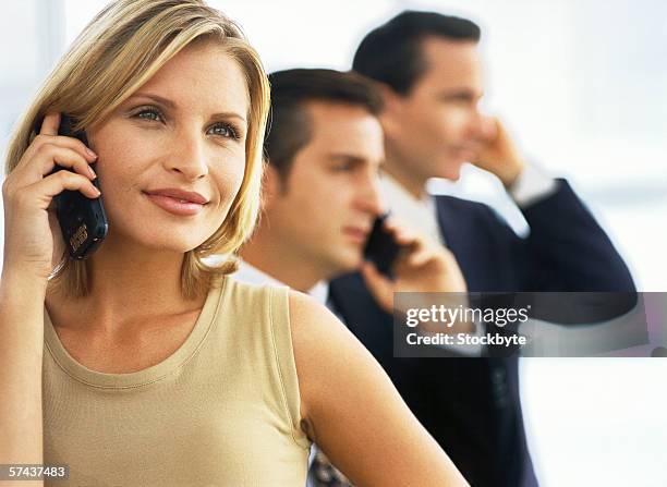 close-up of woman talking on a mobile phone with two men on the phone behind her - 22488btm stockfoto's en -beelden