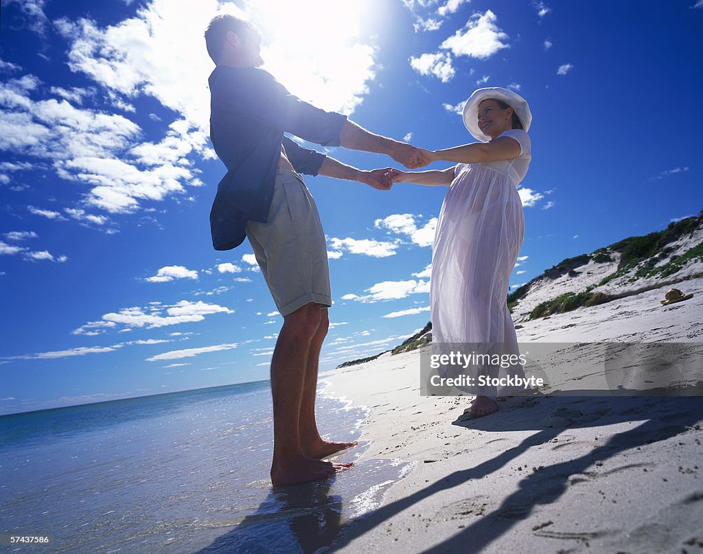 Low angle view of a pregnant woman dancing with a man on the beach