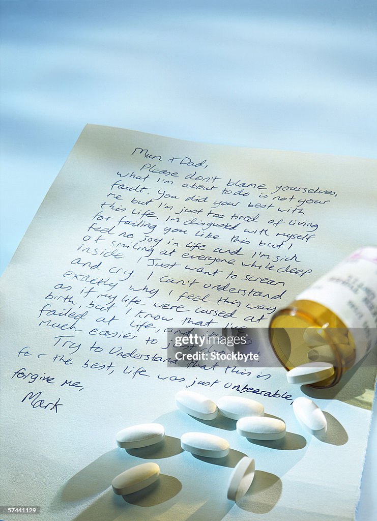 A suicide note with an open vial of medical pills