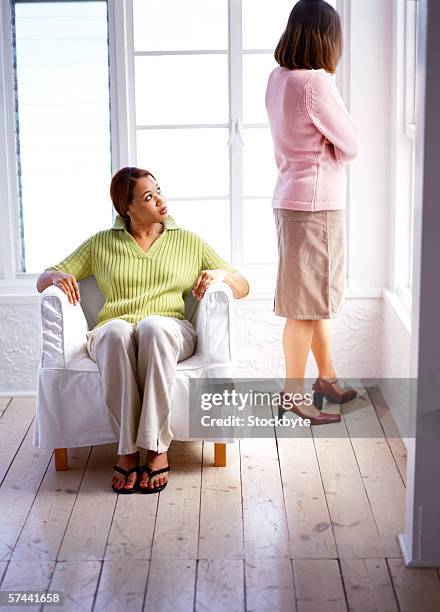 a young gay woman sitting on a couch and her partner standing by a window - dissent collar stock pictures, royalty-free photos & images