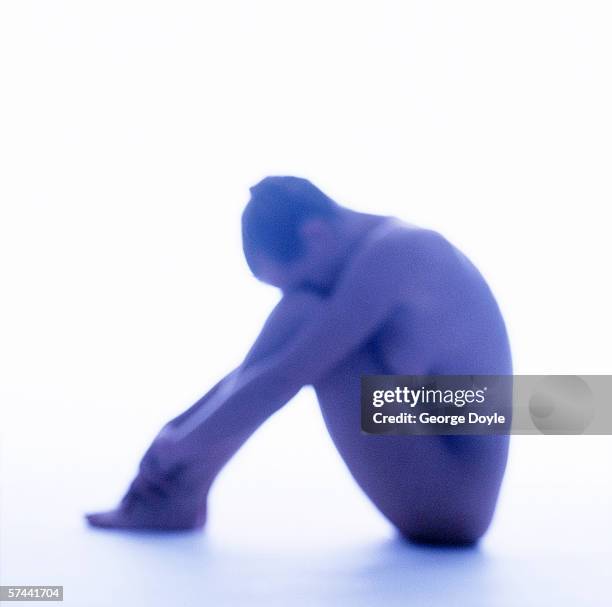 side profile blurred shot of a nude woman sitting on the floor with her face between her knees (tungsten) - studio shot lonely woman stock-fotos und bilder