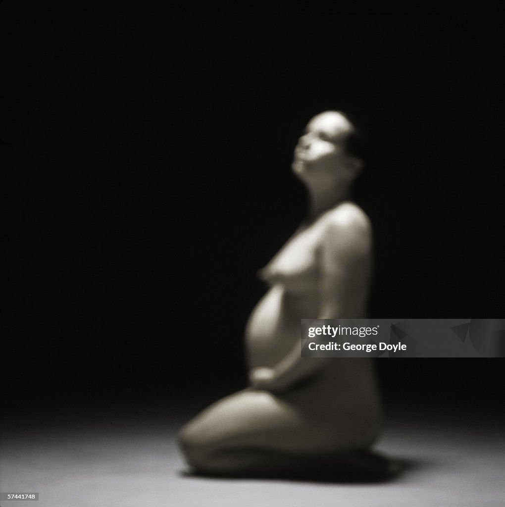 Blurred shot of a nude pregnant woman sitting on the floor