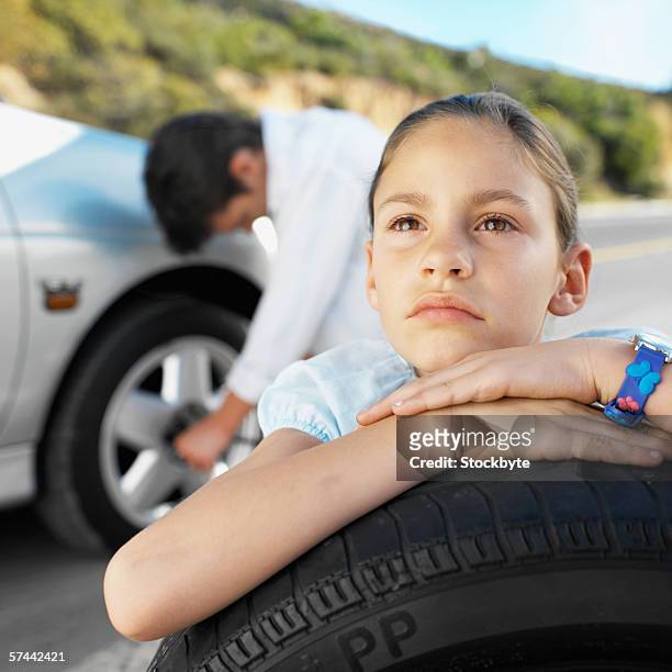 girl (8-9) leaning on a tyre while her father changes the flat tyre - flat tyre stockfoto's en -beelden