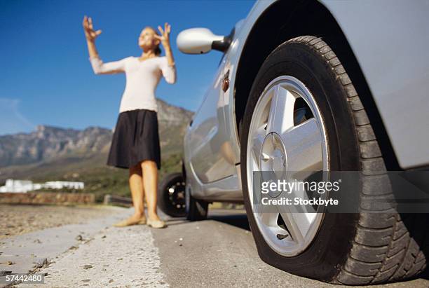 low angle view  of a car with a flat tyre and a woman - flat tyre stockfoto's en -beelden