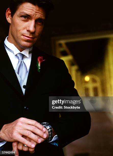 portrait of a young man in a tuxedo looking at his watch - impatience flowers stock-fotos und bilder