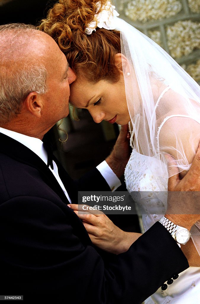 Side view of a father kissing her daughter in her wedding gown