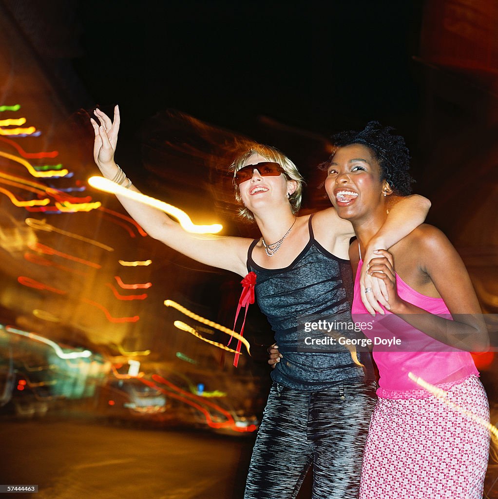 Low angle side profile of two women trying to hail a taxi at night